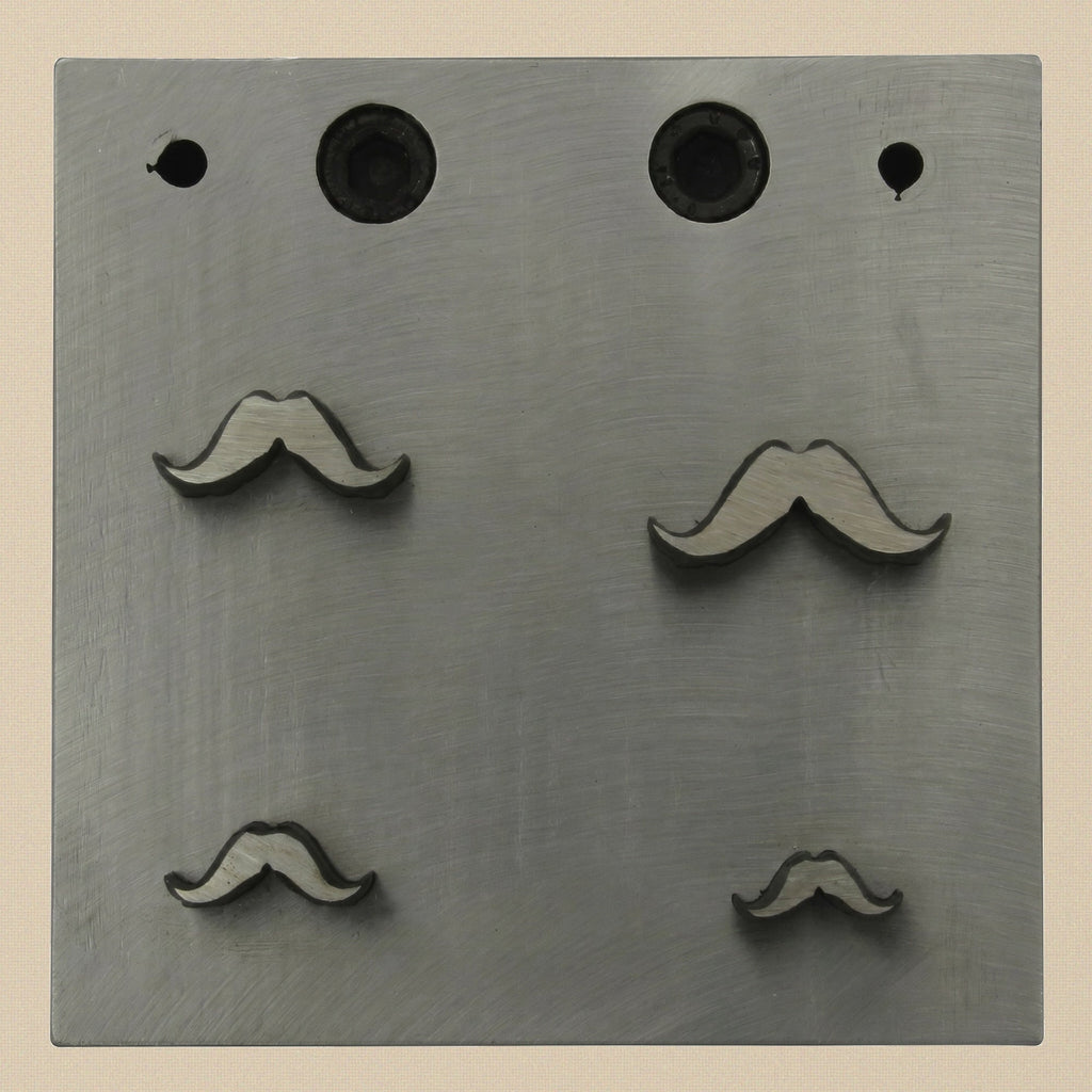 Close-up of the four mustache-shaped apertures in the 76mm square steel die block.