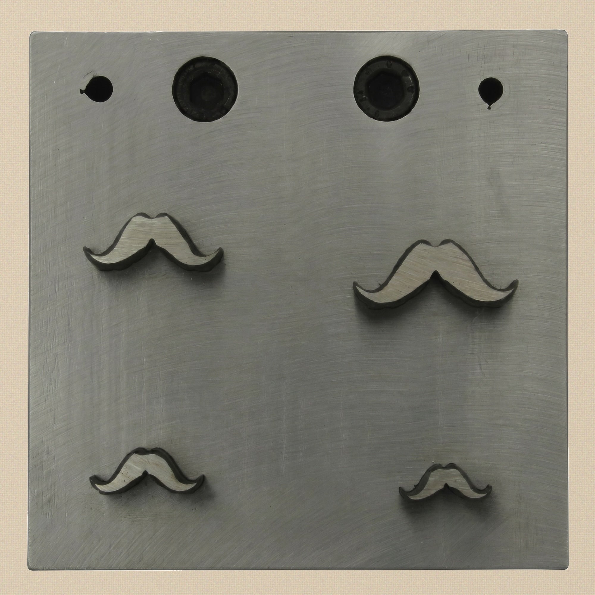 Close-up of the four mustache-shaped apertures in the 76mm square steel die block.