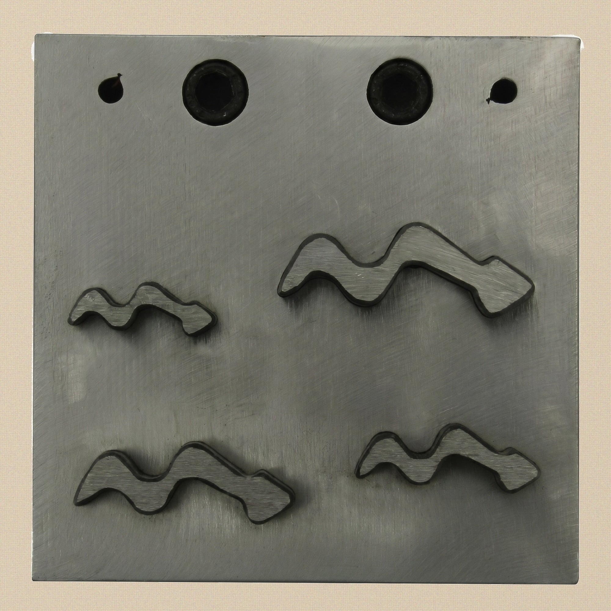 The hardened steel die block showing the four snake-shaped cutting apertures.