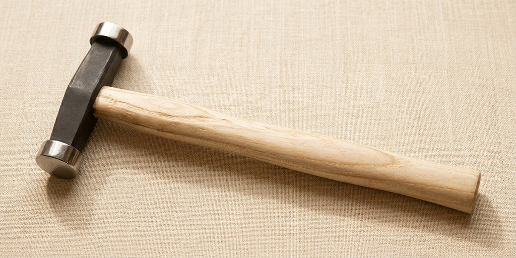 Close-up of the polished steel hammer head and comfortable wooden handle of the planishing hammer.