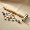 Metal texturing hammer with wooden handle and 18 patterned interchangeable faces for jewellery making.